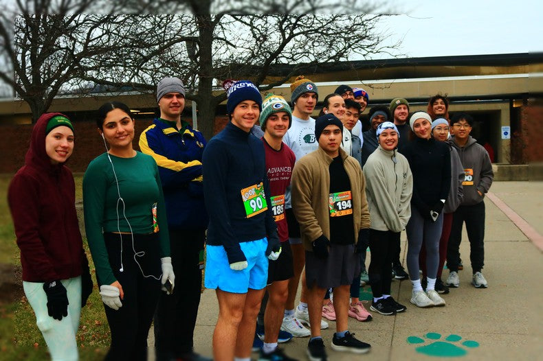  group of students from Binghamton University’s HWS 222 Marathon Training class poses together outside the West Gym before their semester-end half marathon, bundled up for the chilly weather and ready to celebrate their months of preparation and hard work